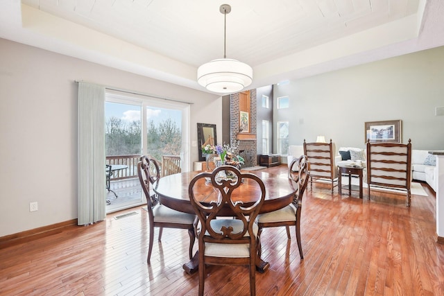 dining room featuring light wood-style floors, a brick fireplace, visible vents, and baseboards