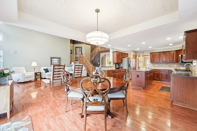 dining space featuring stairs, a tray ceiling, light wood-style flooring, and recessed lighting