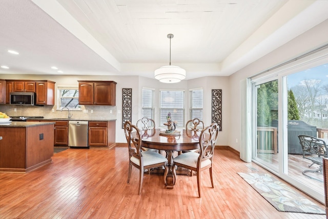 dining area with light wood-style flooring, a tray ceiling, baseboards, and recessed lighting