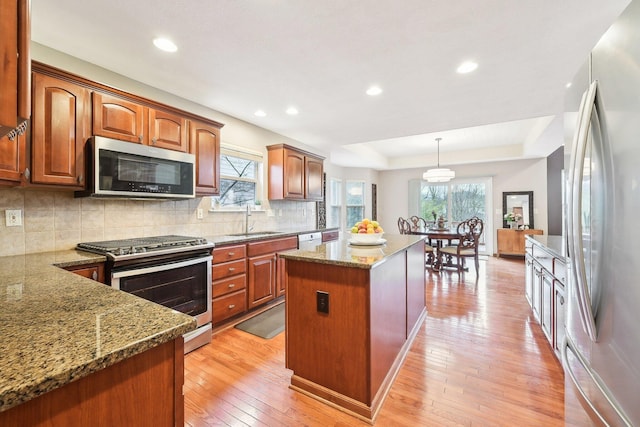 kitchen with light wood-type flooring, dark stone counters, stainless steel appliances, and a sink