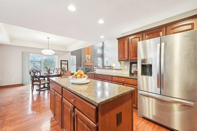 kitchen with light wood-style flooring, a tray ceiling, a kitchen island, and stainless steel refrigerator with ice dispenser