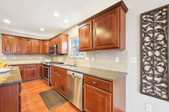 kitchen with a sink, light wood-style floors, appliances with stainless steel finishes, backsplash, and dark stone counters