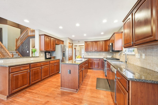 kitchen featuring dark stone counters, appliances with stainless steel finishes, a center island, light wood-type flooring, and a sink