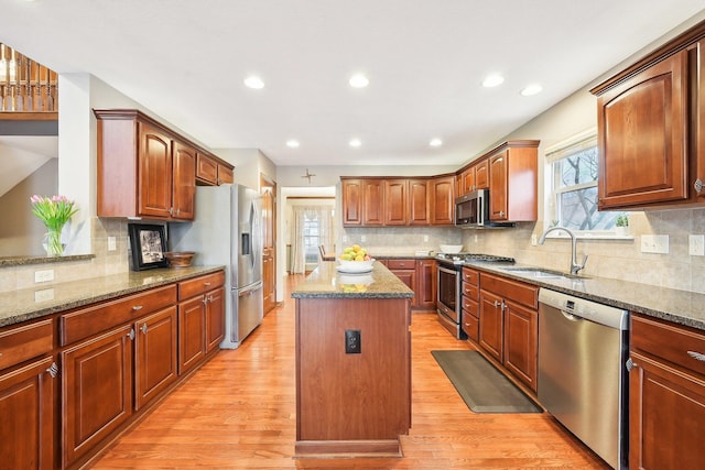 kitchen with appliances with stainless steel finishes, a sink, light wood-style flooring, and a kitchen island