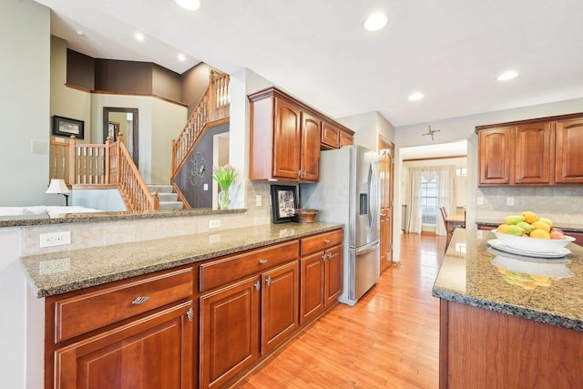 kitchen with light wood finished floors, stainless steel fridge, light stone counters, and decorative backsplash