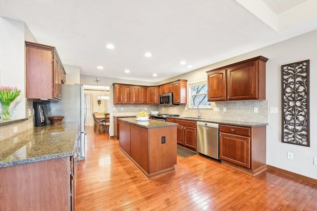 kitchen featuring a center island, tasteful backsplash, appliances with stainless steel finishes, a sink, and light wood-type flooring