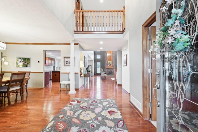 foyer entrance with wood finished floors, visible vents, baseboards, a towering ceiling, and ornate columns