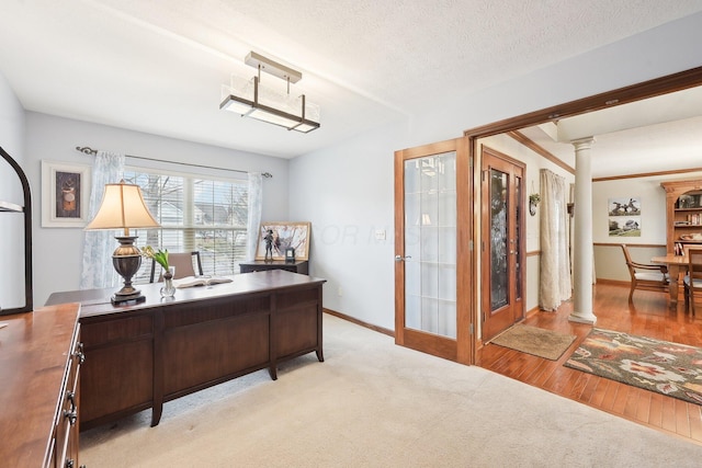 office with baseboards, light wood-style floors, light colored carpet, a textured ceiling, and ornate columns