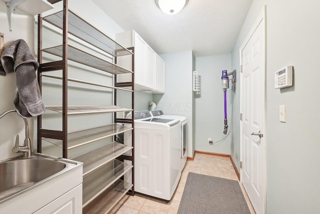 washroom featuring cabinet space, light tile patterned floors, baseboards, washing machine and clothes dryer, and a sink