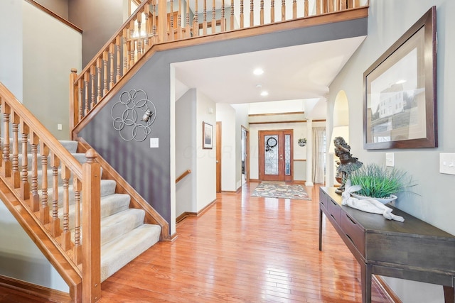 foyer featuring a towering ceiling, stairway, wood-type flooring, and baseboards