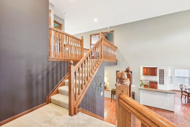 stairs with a high ceiling, recessed lighting, wood finished floors, and baseboards