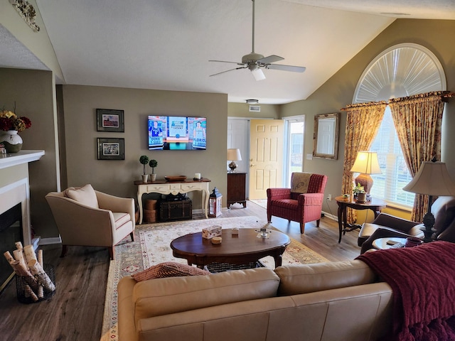 living room featuring lofted ceiling, a fireplace, wood finished floors, a ceiling fan, and baseboards