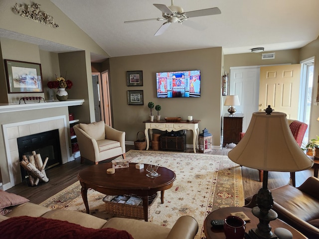 living room featuring ceiling fan, wood finished floors, baseboards, vaulted ceiling, and a tiled fireplace