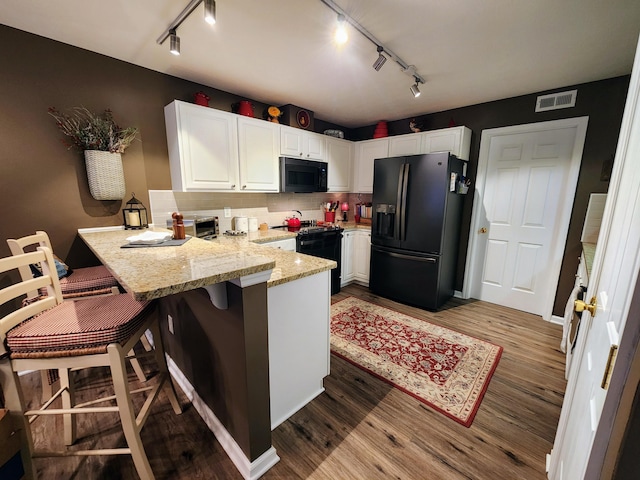 kitchen featuring white cabinets, a peninsula, black appliances, and wood finished floors