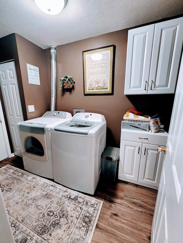 laundry area with a textured ceiling, light wood finished floors, washing machine and dryer, and cabinet space