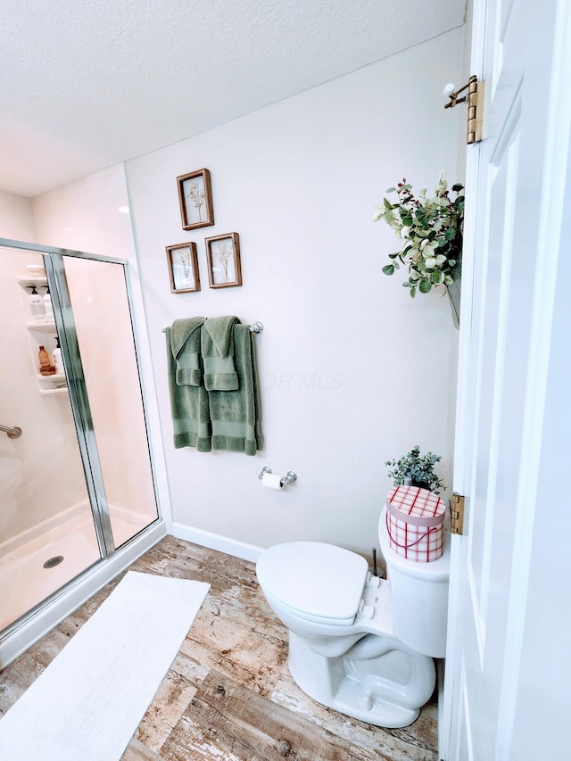 full bath featuring toilet, a stall shower, a textured ceiling, wood finished floors, and baseboards