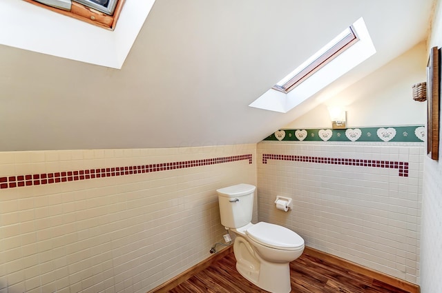 half bathroom with tile walls, lofted ceiling, toilet, wainscoting, and wood finished floors