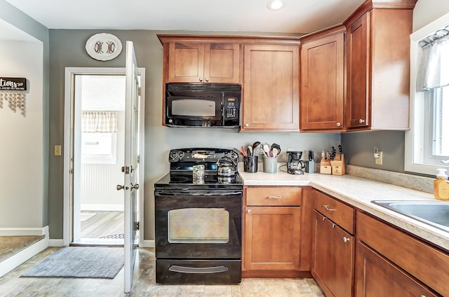 kitchen with black appliances, brown cabinetry, light countertops, and baseboards