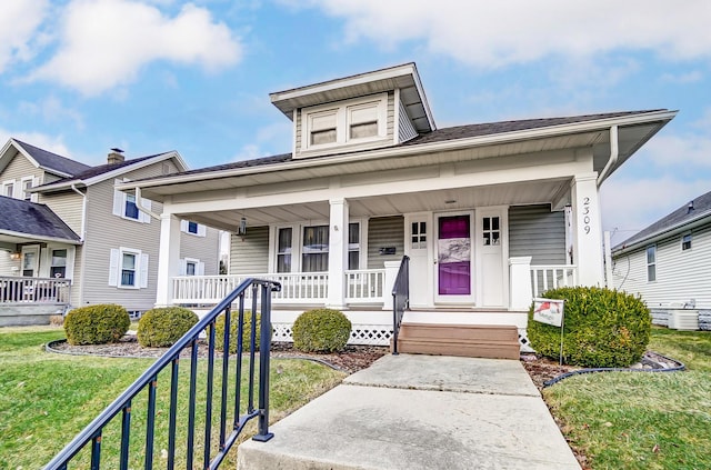 bungalow with covered porch, cooling unit, and a front yard