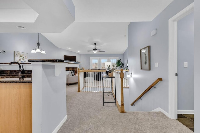 hallway with a notable chandelier, lofted ceiling, light colored carpet, a sink, and an upstairs landing