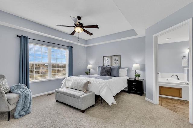 carpeted bedroom with a raised ceiling, visible vents, connected bathroom, ceiling fan, and baseboards