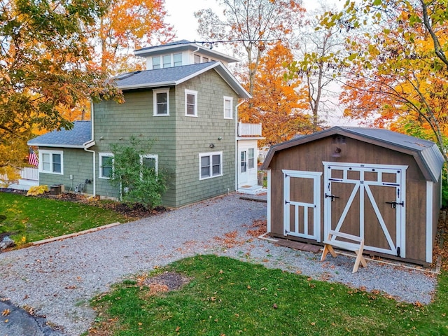 rear view of property featuring driveway, a storage shed, a shingled roof, a lawn, and an outdoor structure