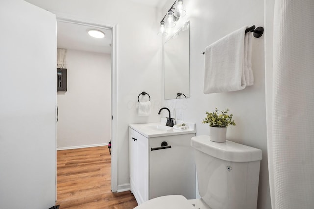 bathroom featuring electric panel, baseboards, toilet, wood finished floors, and vanity