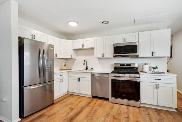 kitchen with light wood finished floors, white cabinets, stainless steel appliances, light countertops, and a sink