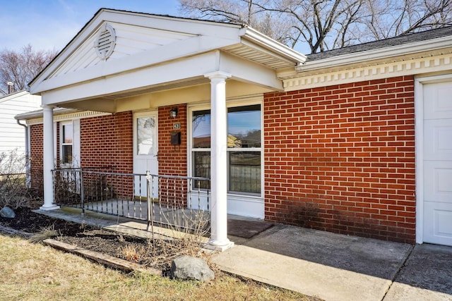 entrance to property featuring an attached garage, covered porch, and brick siding