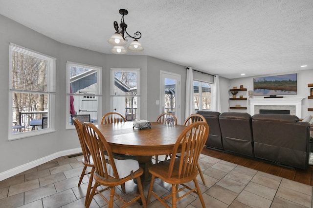 tiled dining area featuring a textured ceiling, a fireplace, a chandelier, and baseboards