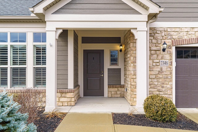 doorway to property with a garage, stone siding, and a shingled roof