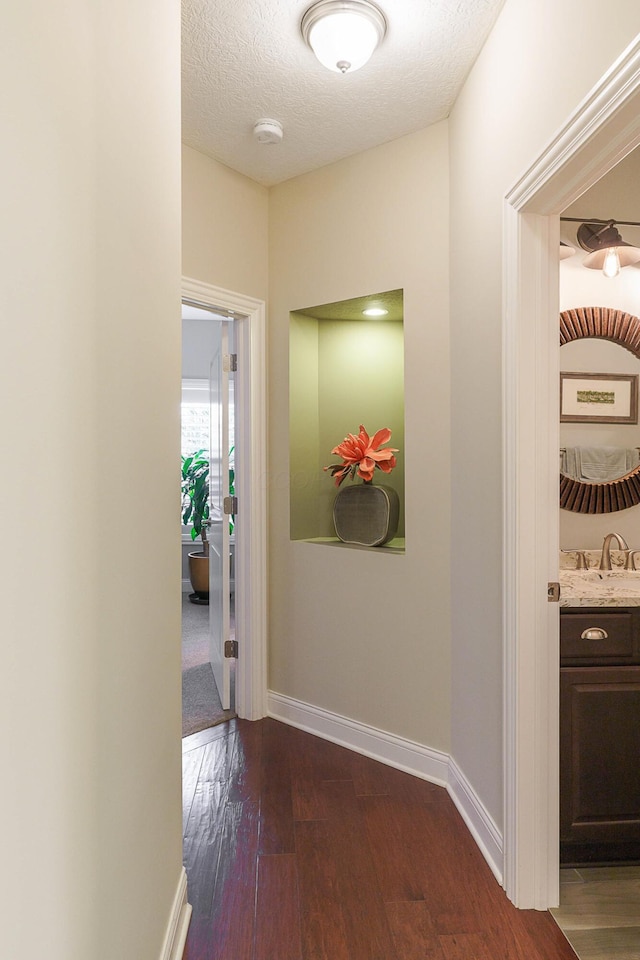 hallway with dark wood finished floors, a textured ceiling, and baseboards