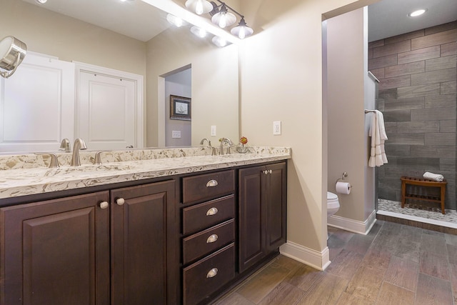 bathroom with toilet, a sink, wood finished floors, double vanity, and walk in shower