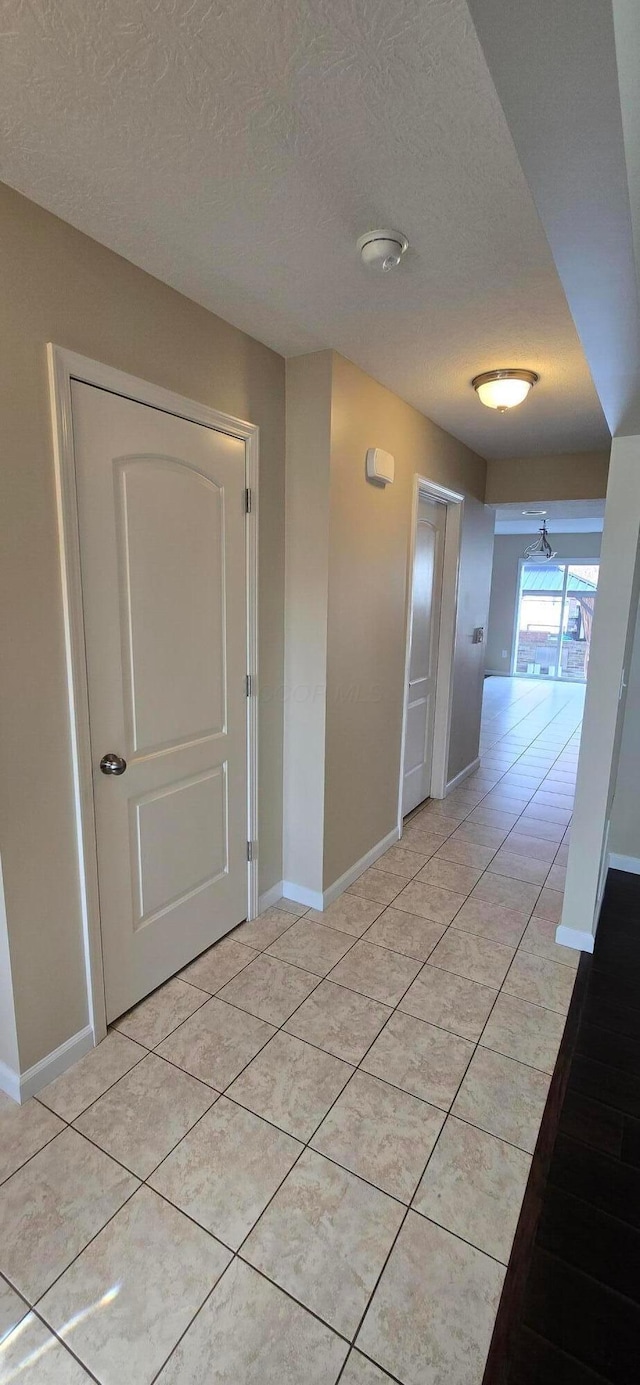 hall featuring light tile patterned flooring, a textured ceiling, and baseboards