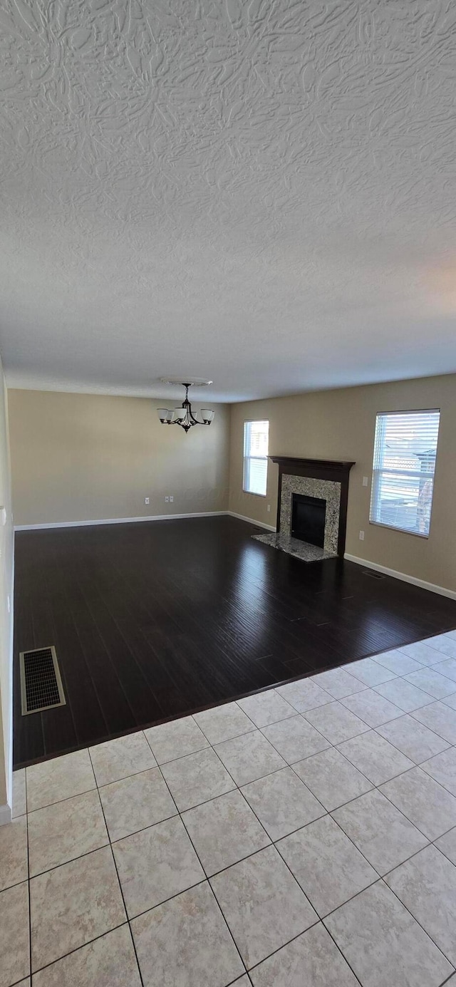 unfurnished living room featuring a fireplace, visible vents, a textured ceiling, baseboards, and tile patterned floors