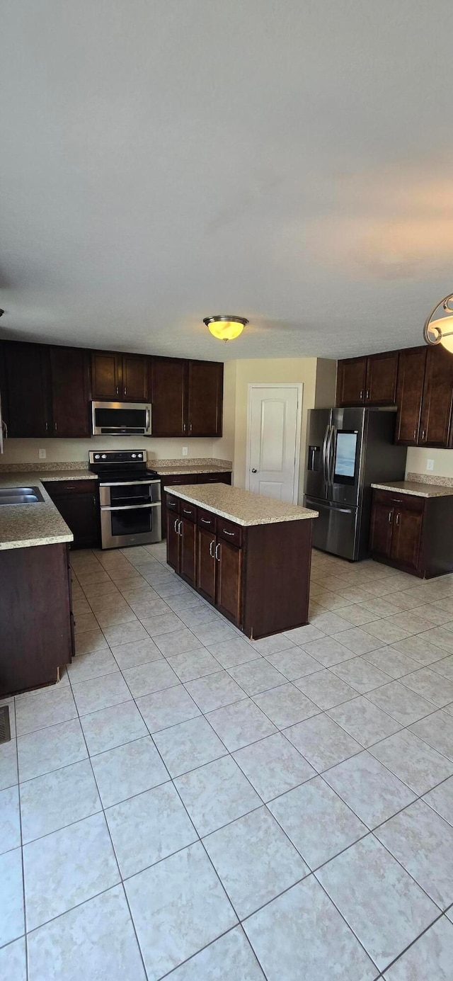 kitchen with light tile patterned floors, a kitchen island, light stone counters, stainless steel appliances, and dark brown cabinets