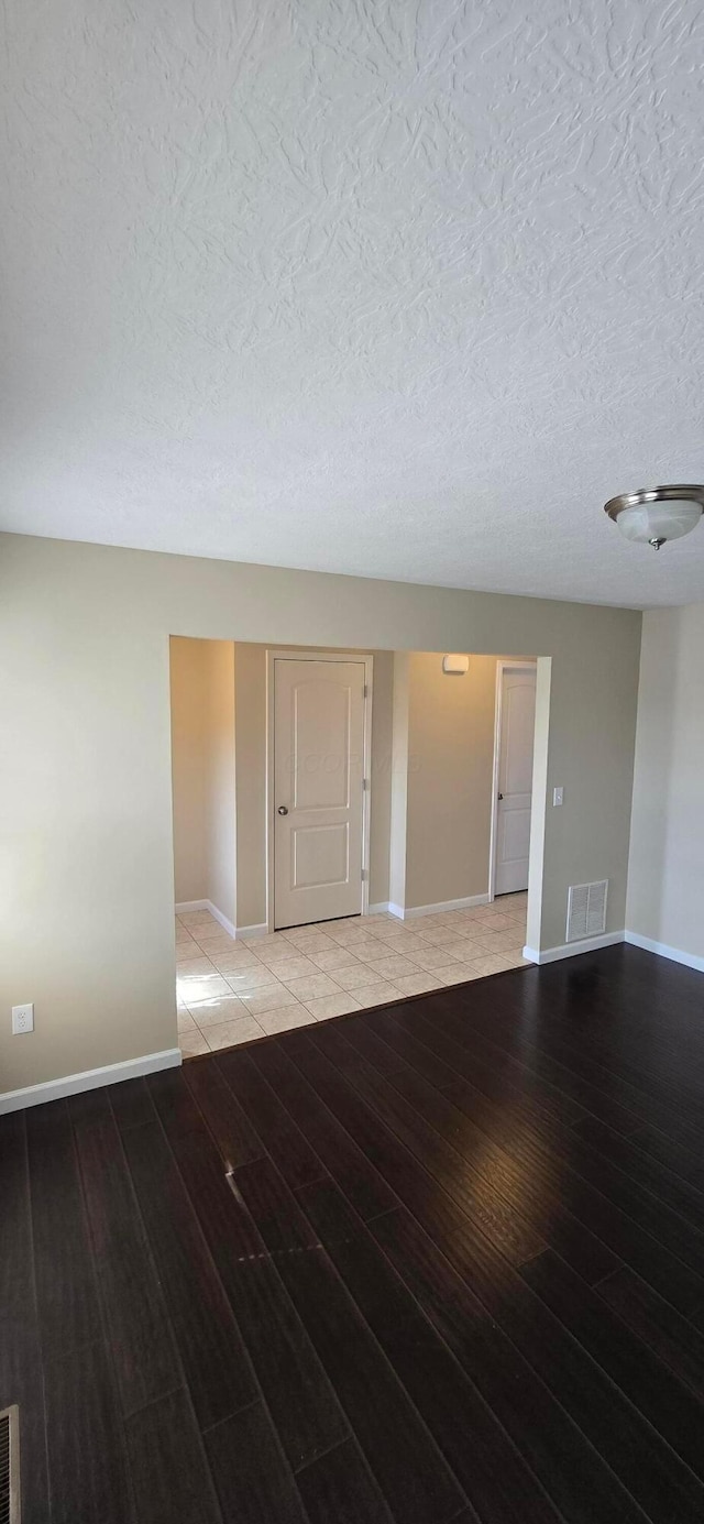 empty room featuring a textured ceiling, light wood-type flooring, visible vents, and baseboards