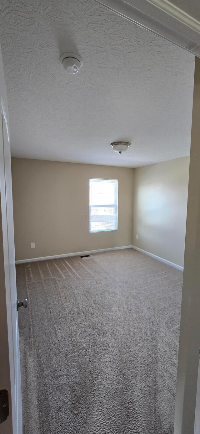 carpeted spare room featuring visible vents, baseboards, and a textured ceiling