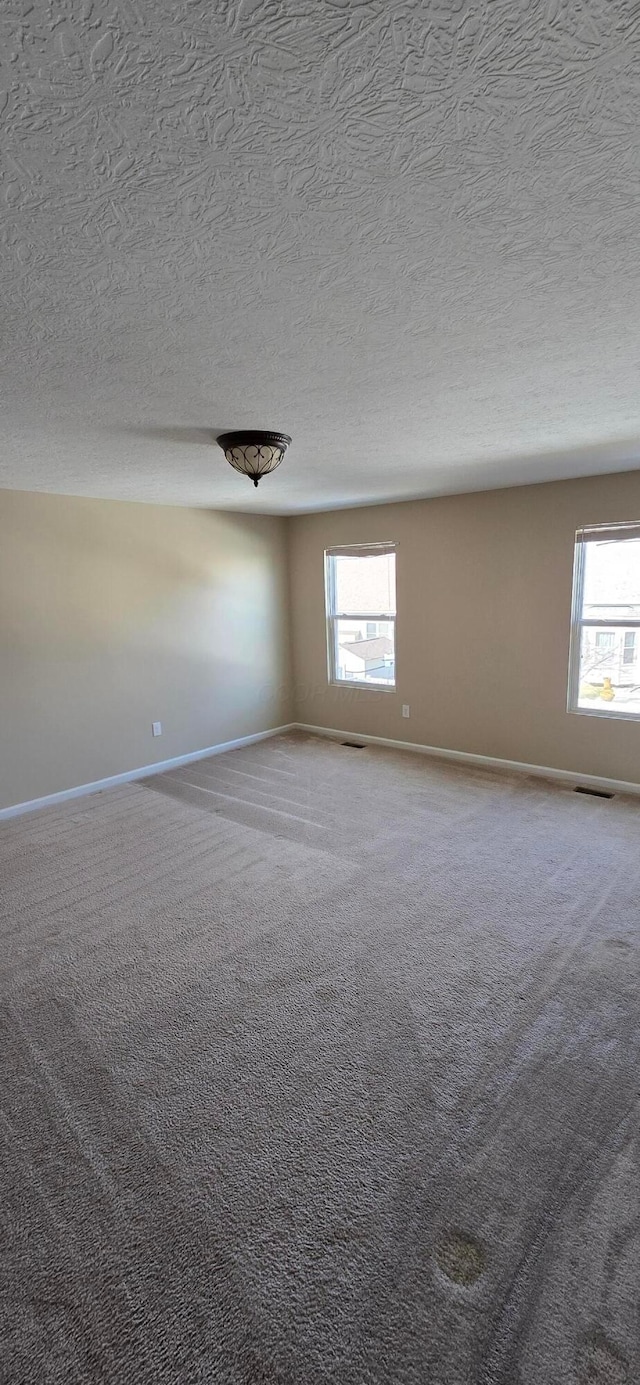 carpeted spare room featuring a textured ceiling, plenty of natural light, visible vents, and baseboards