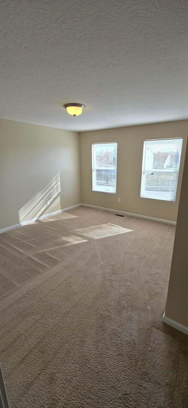 carpeted spare room with a textured ceiling and baseboards