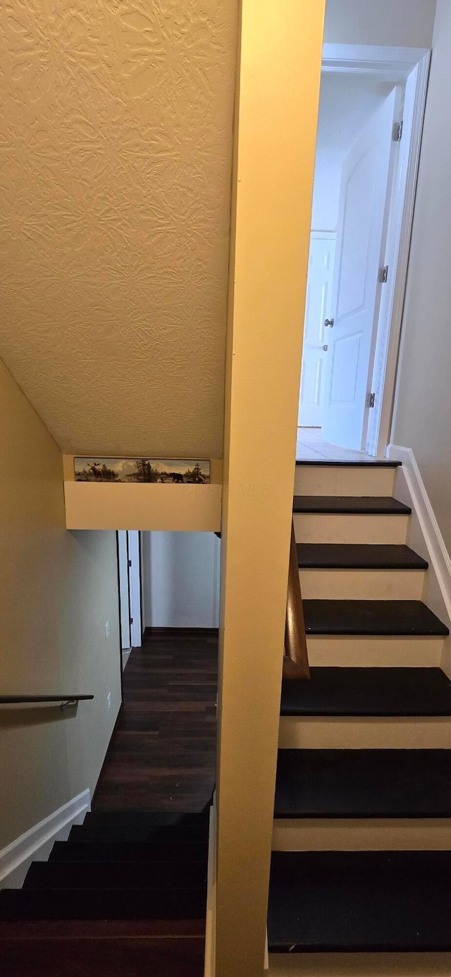 staircase with a textured ceiling and wood finished floors