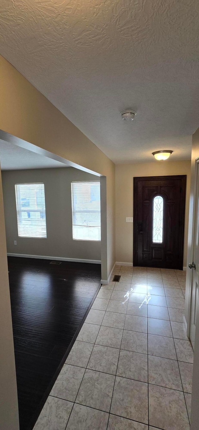 entrance foyer featuring lofted ceiling, a textured ceiling, baseboards, and light tile patterned floors