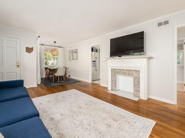 living area with baseboards, visible vents, crown molding, and wood finished floors