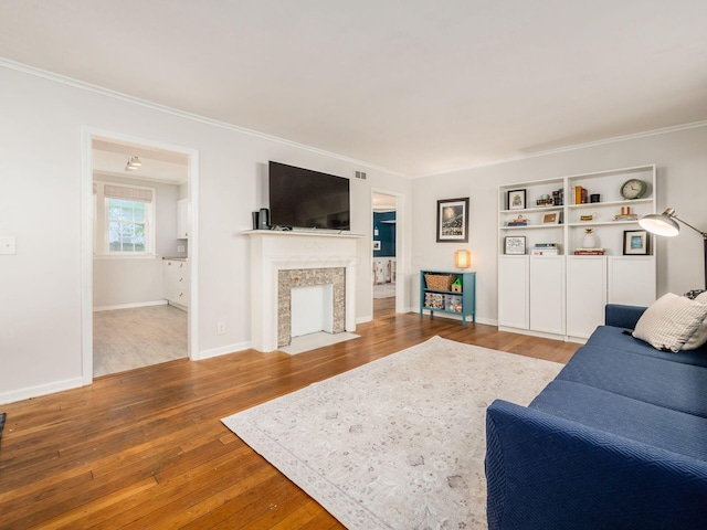 living room with a fireplace with flush hearth, wood-type flooring, ornamental molding, and baseboards