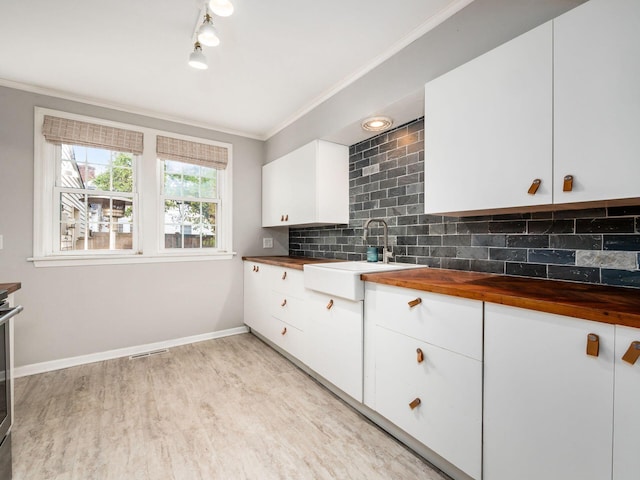 kitchen with butcher block counters, backsplash, light wood-style flooring, ornamental molding, and a sink