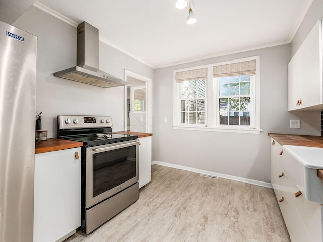 kitchen with stainless steel appliances, butcher block counters, white cabinets, and wall chimney range hood