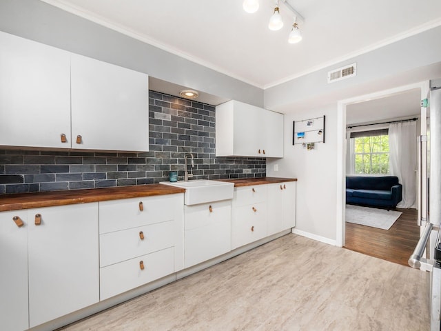 kitchen with visible vents, butcher block counters, a sink, crown molding, and backsplash