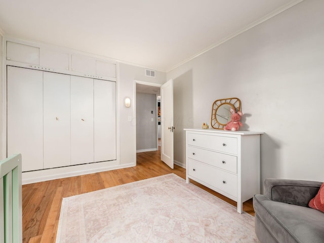 bedroom with light wood-style floors, visible vents, ornamental molding, and baseboards