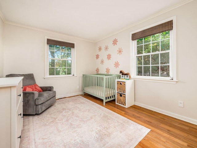 bedroom with visible vents, baseboards, ornamental molding, wood finished floors, and a nursery area