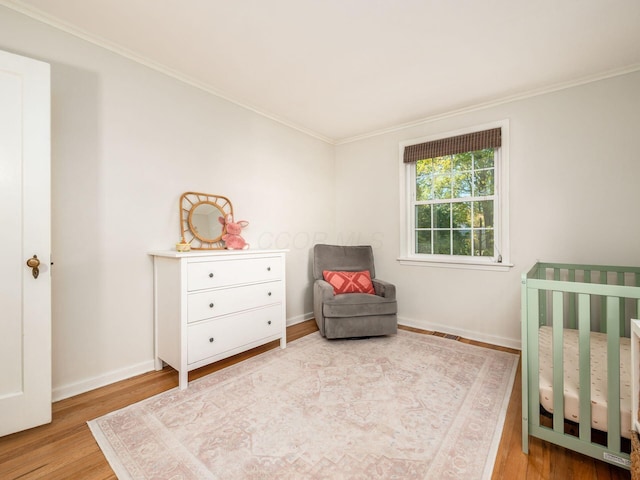 bedroom featuring a nursery area, crown molding, wood finished floors, and baseboards